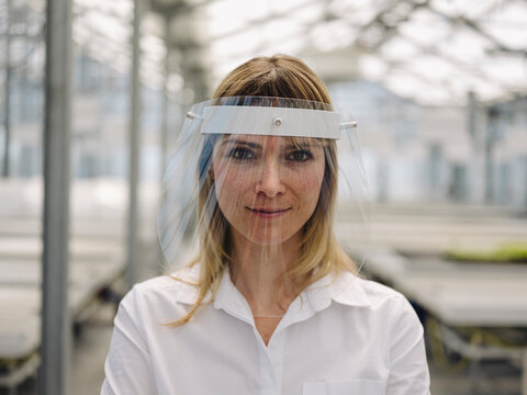 Close-up of confident businesswoman wearing face shield in greenhouse