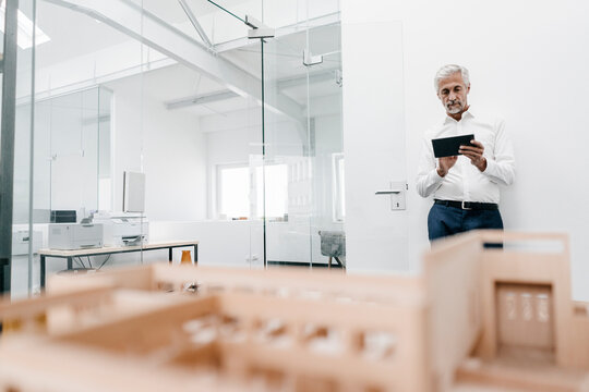 Mature businessman with architectural model and tablet in office