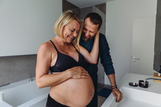 Happy mature pregnant couple watching expectant mother?s belly in bathroom