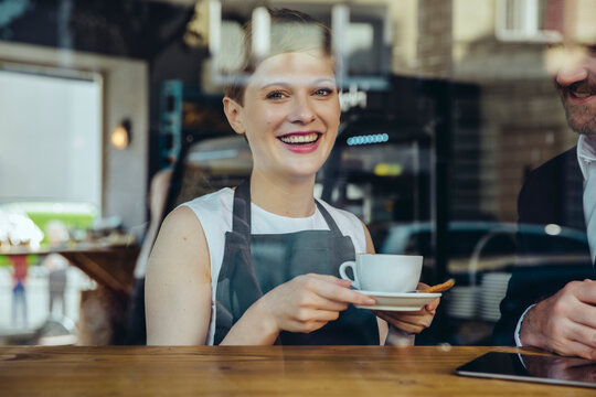Smiling waitress serving coffee to customer in cafe
