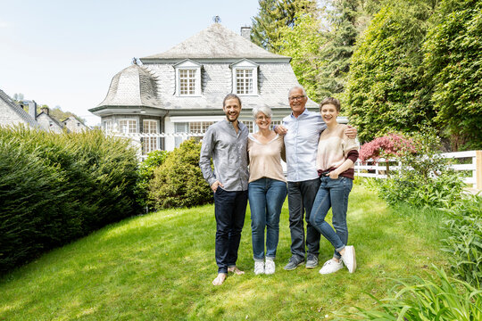 Happy senior couple with adult children standing in garden of their home