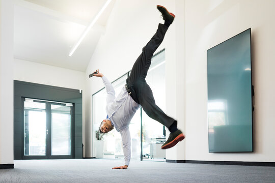 Businessman with cell phone doing a one-handed handstand on office floor