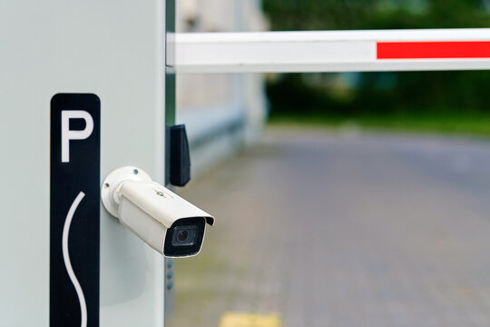 Boom barrier blocking access to private urban territory with surveillance camera mounted on the post for license plate recognition and security monitoring. Parking access control system