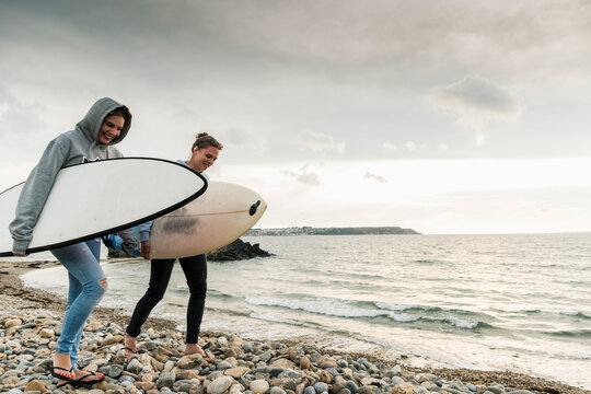 Happy friends with surfboard walking on stony beach