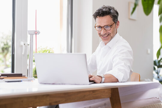 Businessma n sitting in office, using laptop, looking at model of a windwheel
