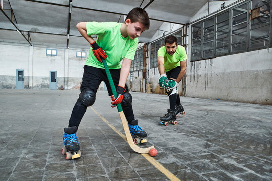 Boy practicing roller hockey with father on court