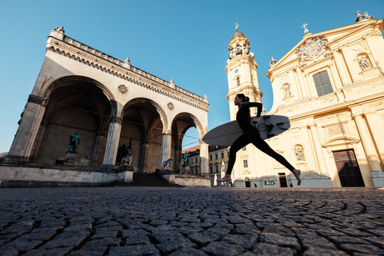 Young woman with surfboard on the way to Eisbach, Munich, Germany