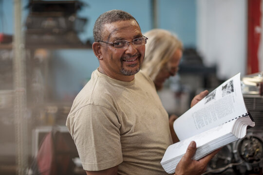 Portrait of smiling mechanic in workshop holding book