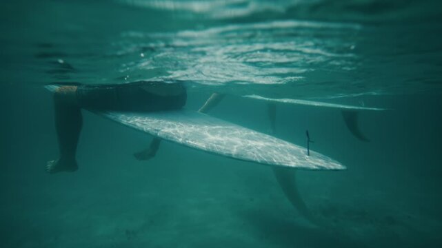 Underwater fifty fifty half and halfof surfers sitting in calm turquoise ocean near the surface