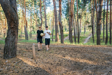 Obraz premium Two Teenage Friends Walking in Sunny Pine Forest Holding Soccer Ball and Using Smartphone for Leisure Activity