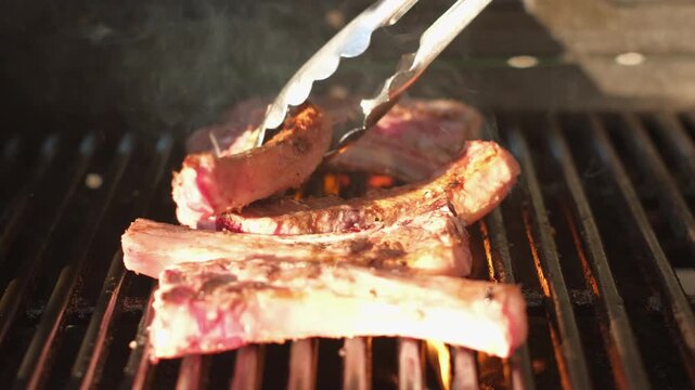 Sizzling lamb chops turned with tongs on hot barbecue and then seasoned