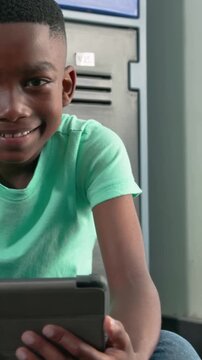 Vertical video: Looking down boy holding tablet and reacting in school locker C15, mint tee, jeans