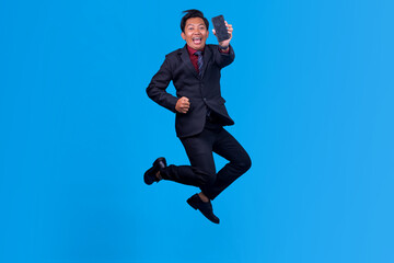 Obraz premium Full Body Shot Of Happy Asian Businessman Jumping For Joy While Holding Smartphone