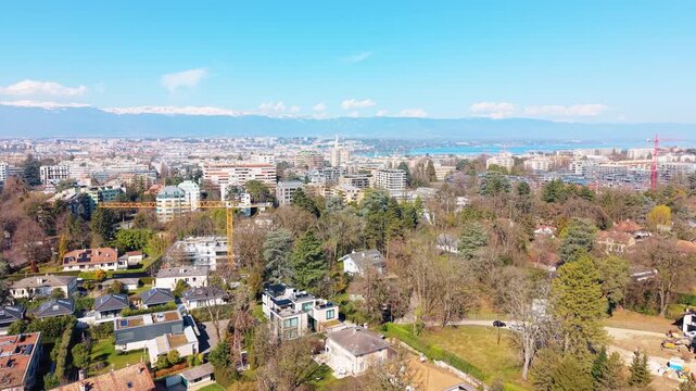Aerial: Geneva cityscape from Conches with Lake Geneva and water fountain during the day in Canton of Geneva, Switzerland, jib up drone shot