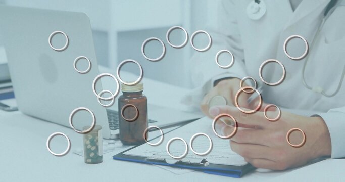 Doctor wearing white lab coat, stethoscope holding pill bottle, checking labels at desk with laptop