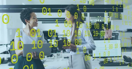 Talking two women in business attire gesturing over laptop at open office with yellow binary digits