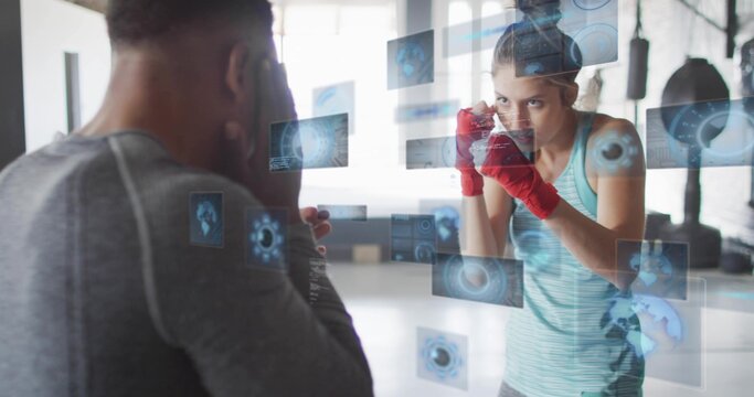Training female boxer wearing tank top and red hand wraps with coach in gym, holographic HUD