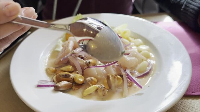 Unrecognizable person eating Peruvian ceviche with a spoon in a restaurant