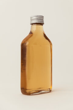 Small glass pocket flask bottle with silver screw cap filled with amber liquid or liquor, isolated on a light neutral background. Flat medicine or spirit bottle for branding and product design.