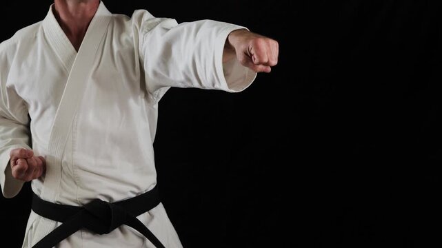 A professional male athlete in karate practices punches and blocks with his hands on a black background