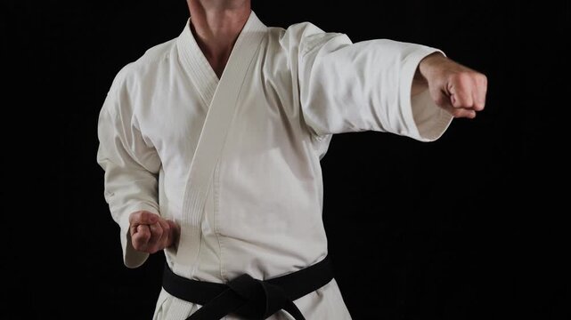 A professional male athlete in karate performs punches and blocks with his hands on a black background