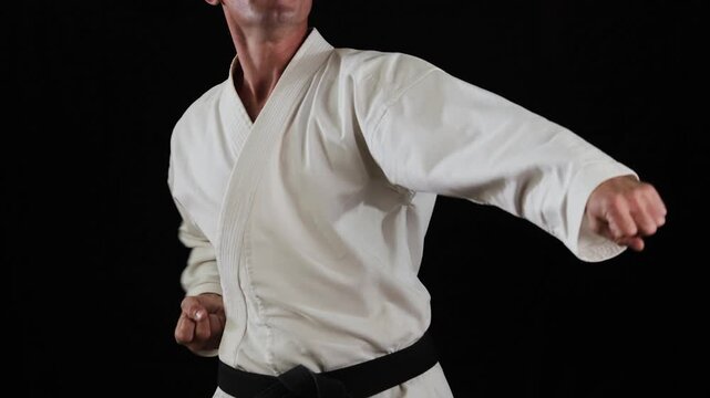 A professional male athlete in karate performs punches and blocks with his hands at a high pace on a black background