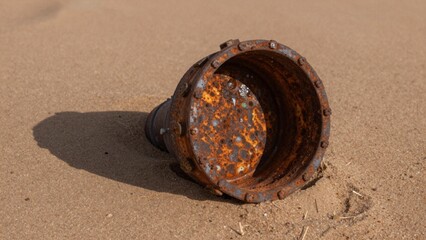 Rusted cylindrical object lying sandy beach appears made metal has weathered aged appearance patches rust cove