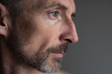 Obraz premium Close-up portrait of an adult man with an emotionless stare against a gray backdrop