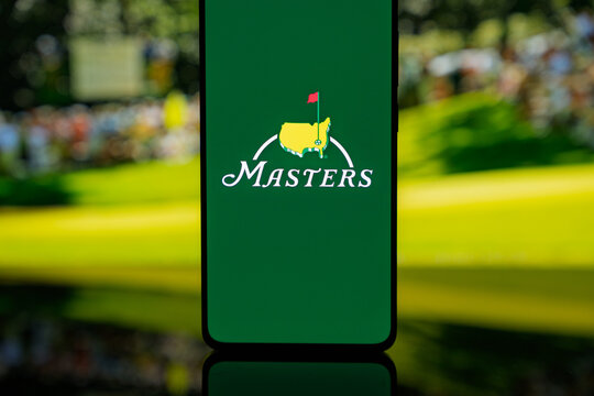 Smartphone displaying The Masters golf tournament logo on a green screen, set against a blurred background, representing professional sports media and tournament coverage