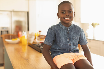 African American child sitting on wooden island in kitchen near stove in denim shirt orange shorts © wavebreak3