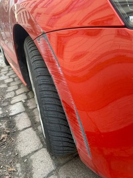 Kratzer und Lackschaden an einem roten Auto an Kotfl&uuml;gel und Sto&szlig;stange. Detailaufnahme eines Parkremplers, Konzept f&uuml;r Autoschaden, Versicherung, Reparatur und Unfall im Stra&szlig;enverkehr.