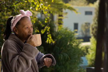 Senior Chinese woman standing on balcony sipping from pale-pink ribbed mug near railing, copy space © wavebreak3
