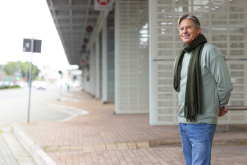 Senior man standing on covered walk hands behind back wearing sweater scarf and jeans, copy space © wavebreak3