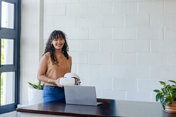 African American woman holding white VR headset standing at home office with open laptop and plants © wavebreak3