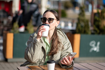 Fototapeta premium Young woman in sunglasses enjoying sun with coffee at outdoor cafe