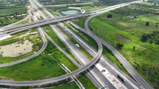 Aerial view of modern highway interchange with multilayer roads and curved ramps surrounded by green farmland, showcasing transportation infrastructure, urban development, and road network planning.
