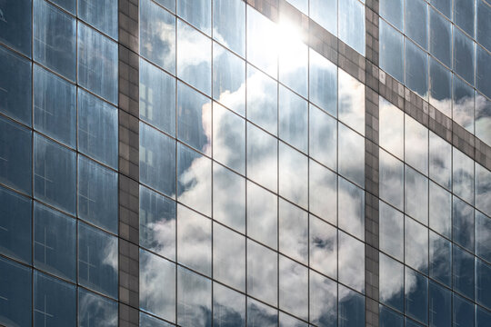 Soft clouds mirror on repeating glass windows of a modern corporate facade forming an architectural pattern against blue sky for office building background