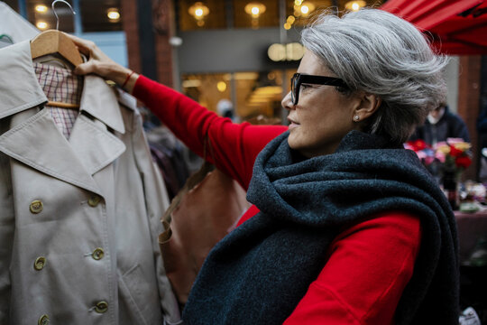 Woman choosing trench coat at street market in urban setting