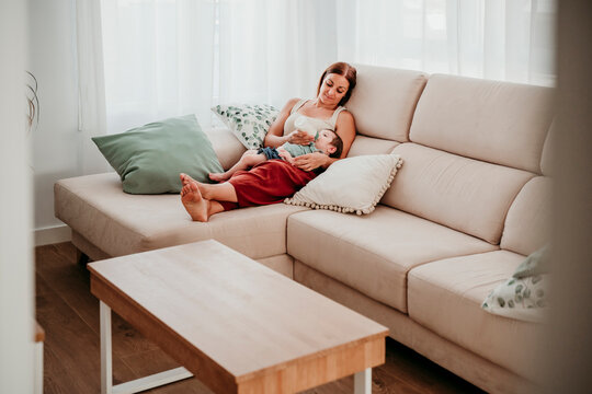 Mother bottle feeding baby on sofa enjoying quality time at home