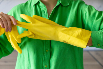 A woman in green clothes taking off yellow protective gloves. After cleaning concept