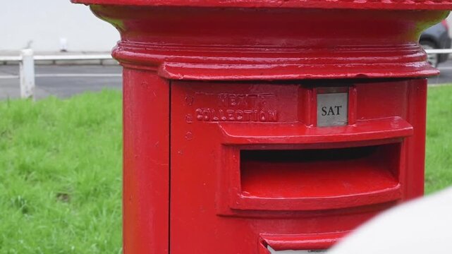 Male hand postcard into red british post box on the street. Concept of communication tradition postal service business
