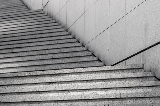 Monochrome interior staircase of concrete steps with a handrail in minimal architecture showing texture and parallel lines with quiet modern mood