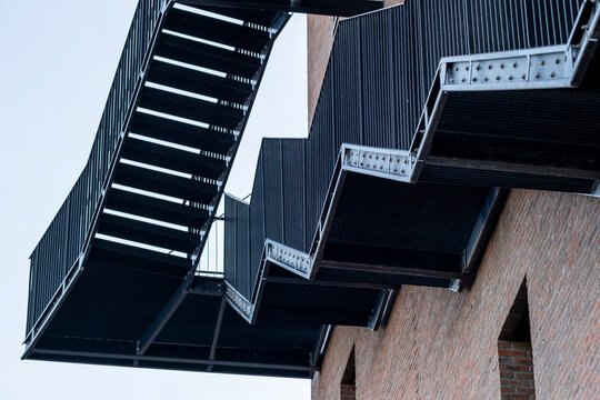 Metal fireescape staircase on an urban building creates industrial structure lines with dramatic perspective showing exterior architecture details against sky