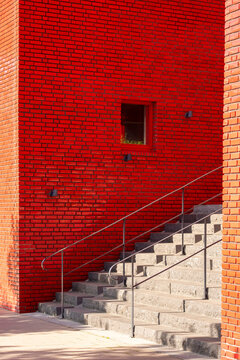 Concrete steps rise along a bold red brick wall with a clean handrail staircase forming minimal exterior architecture geometry with crisp shadows
