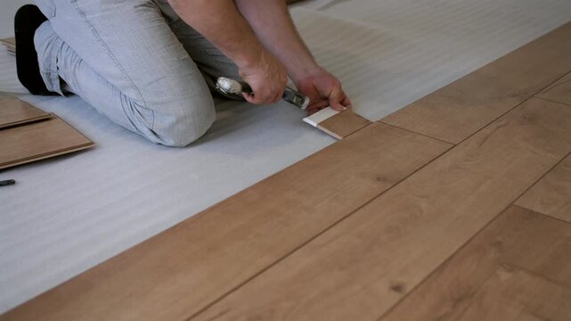 Worker aligning and clicking laminate floor panels together. Interior renovation and flooring installation process.