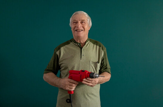 Smiling man indoors holding drill against green background