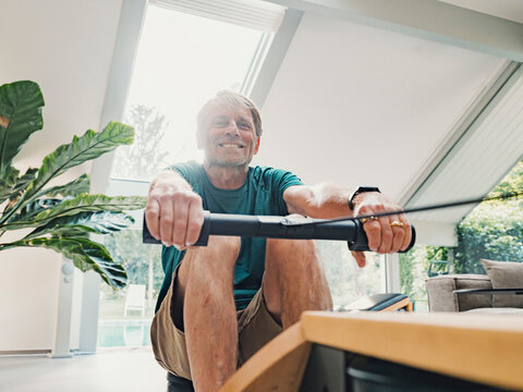 Man working out on rowing machine at home in living room with health tracker