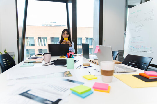 Manager seated at table in office looking at smartphone during meeting