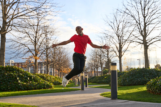 Smiling man jumping joyfully in a park on a sunny day