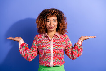 Confident mixed race young woman poses with open hands against blue background wearing a colorful...